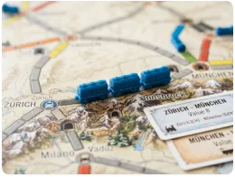 Fragment planszy do gry o pociągach z niebieskimi figurkami lokomotyw na trasie